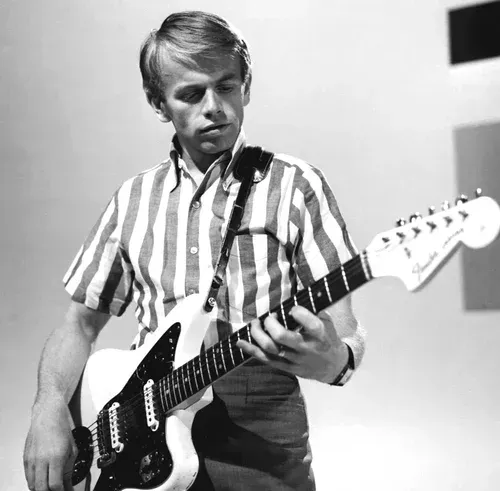 Man playing an electric guitar in a striped shirt, looking down at the instrument.
