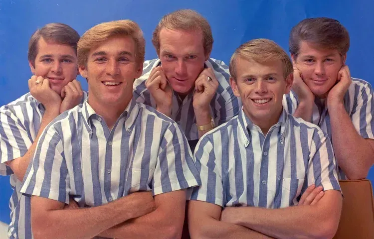 Five smiling young men in blue-and-white striped shirts pose closely together against a plain background.
