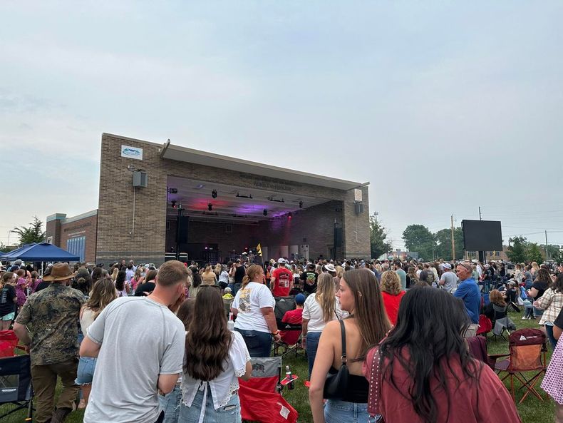 Outdoor concert crowd facing a large stage with purple lighting under a cloudy sky