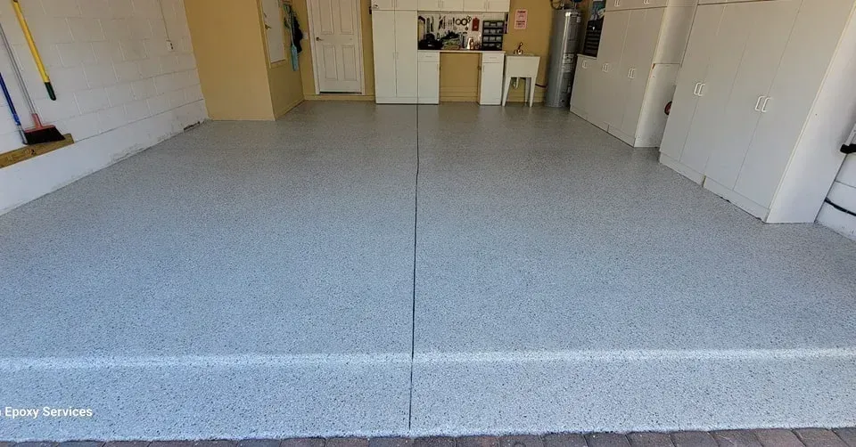 Garage with a gray epoxy floor. Walls are white and beige with closed cabinets and door in the background.