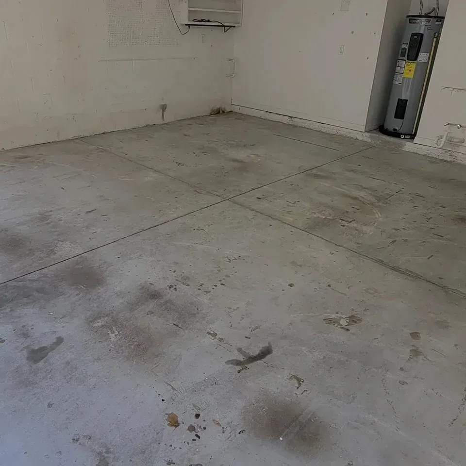 Concrete garage floor with stains, water heater, and ventilation unit.
