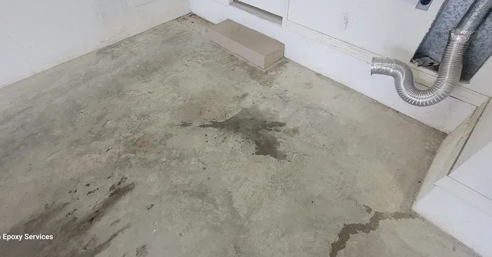 Concrete floor stained with water, near a wall and appliance vent.