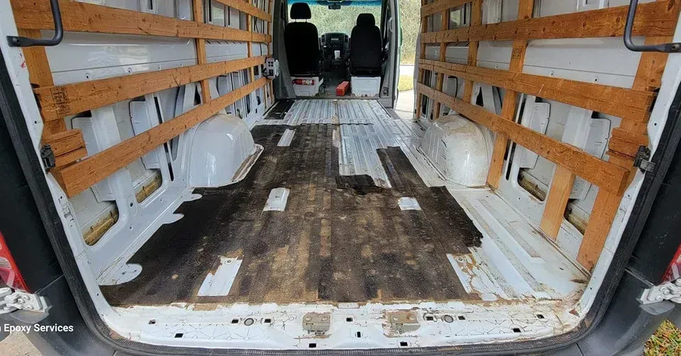 Inside of a cargo van, showing wooden shelving and stained floor.