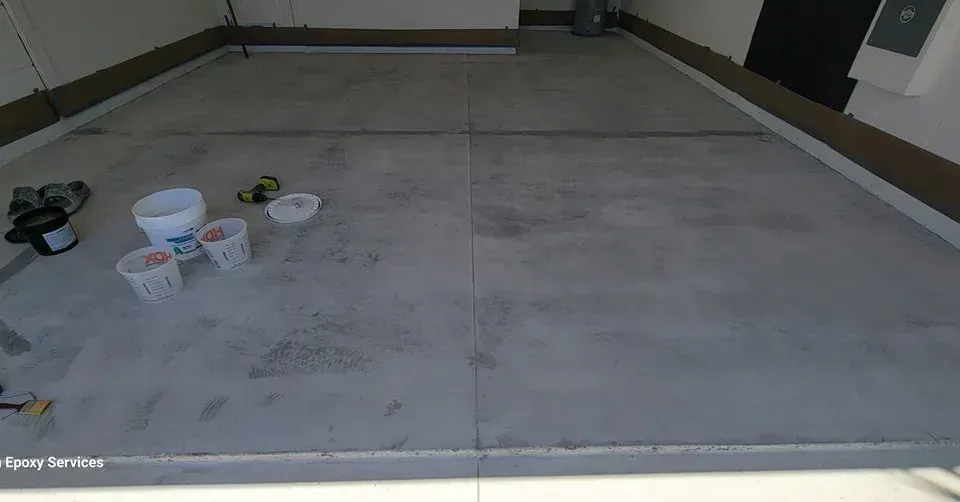 Concrete garage floor with buckets and paint supplies.