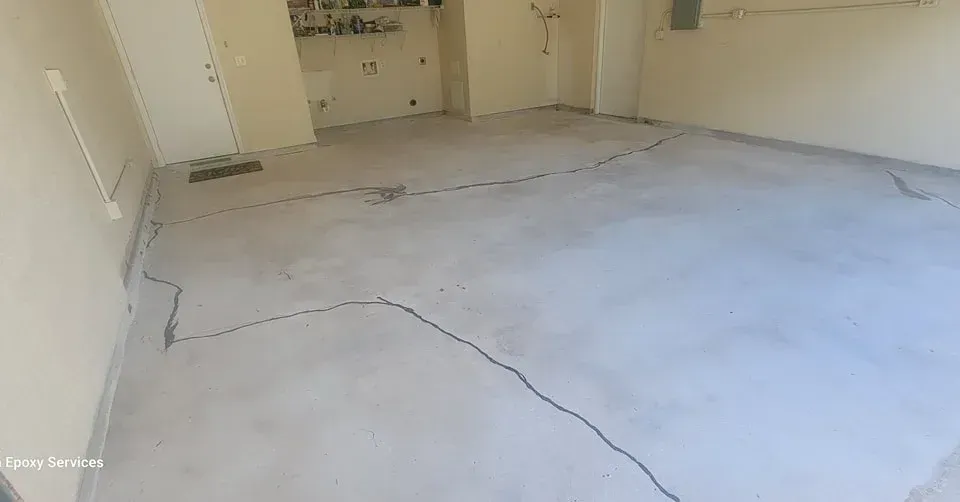 Empty garage with light gray concrete floor, visible cracks, and beige walls.