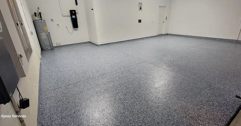 Empty garage with a speckled blue and gray epoxy floor, white walls, and a water heater.