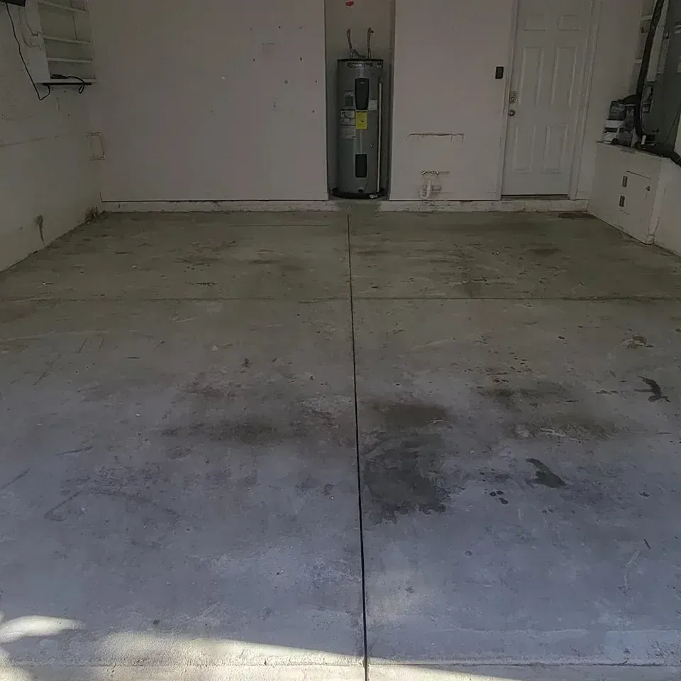 Empty concrete garage interior with water heater, door, and AC unit.