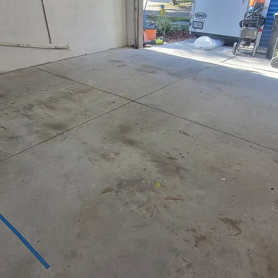 Concrete garage floor with dirt stains and a few scattered items.