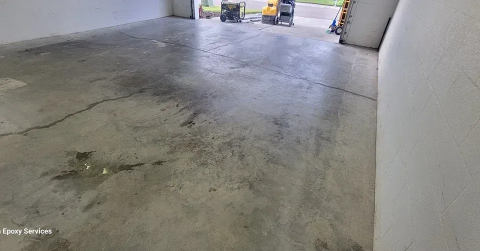 Concrete floor of a garage, with some water stains and cracks. Machinery is visible at the open doorway.