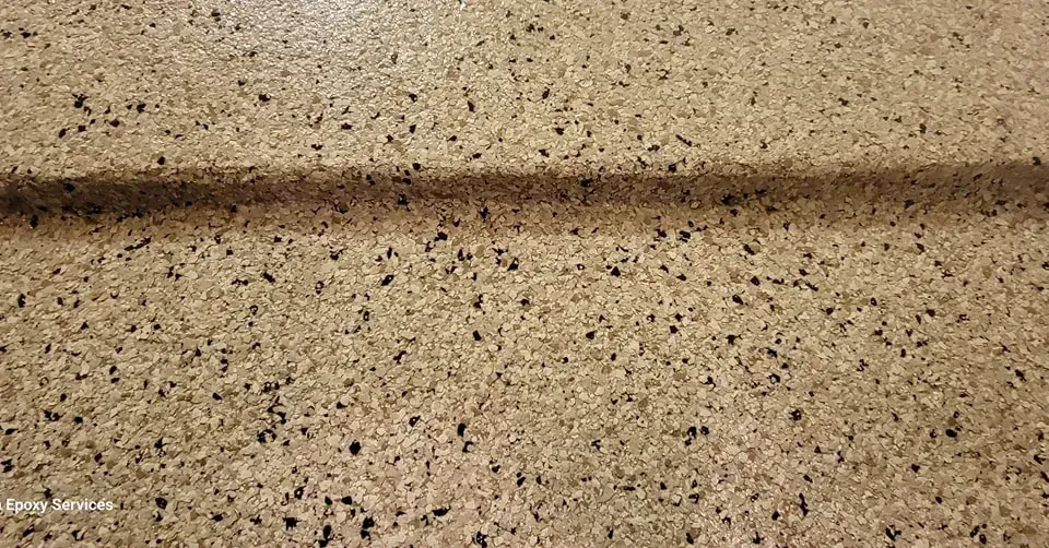 Tan, speckled concrete floor with a dark line casting a shadow across it.
