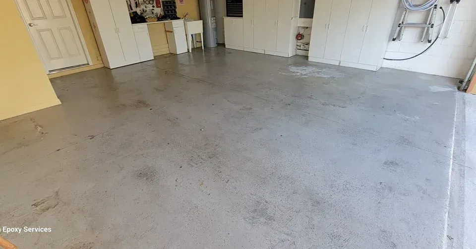 Gray concrete garage floor, showing a utility sink and white cabinetry in the background.