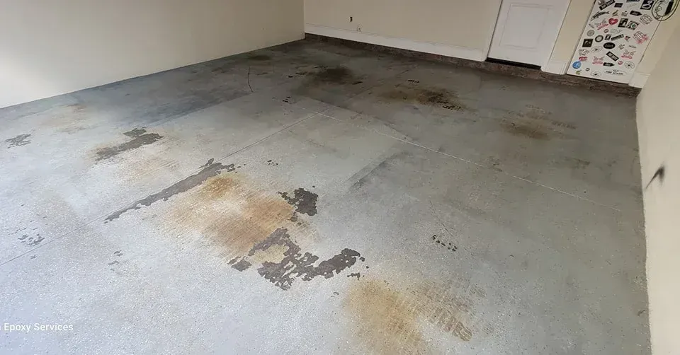 Garage floor with stains, showing areas of worn, gray concrete.