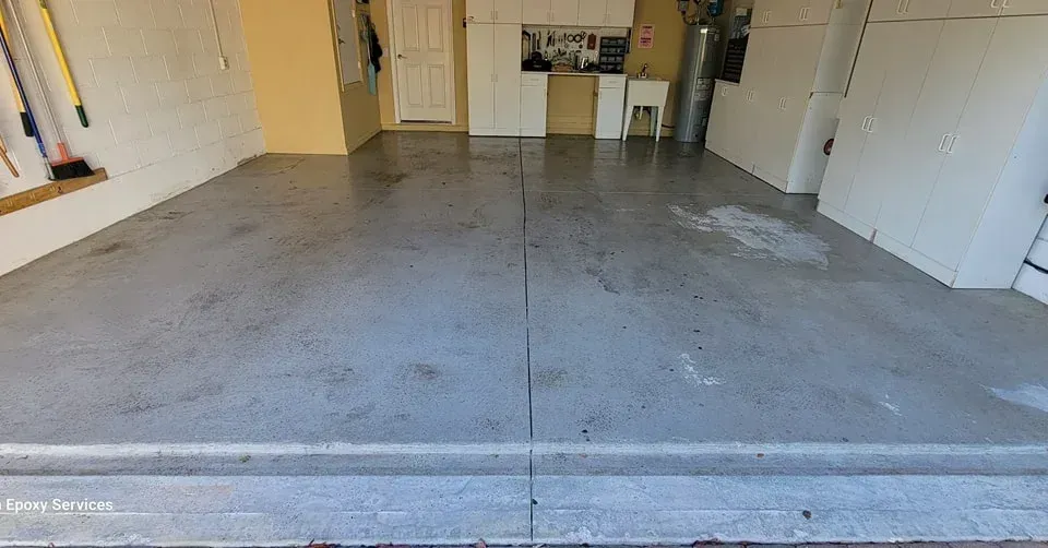 Garage interior with gray painted concrete floor, cabinets, door, and a utility sink.