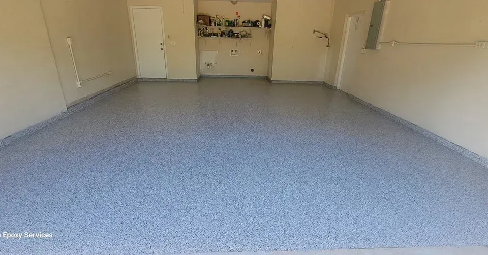 Garage with a blue and gray speckled epoxy floor, light walls, and a door in the back.
