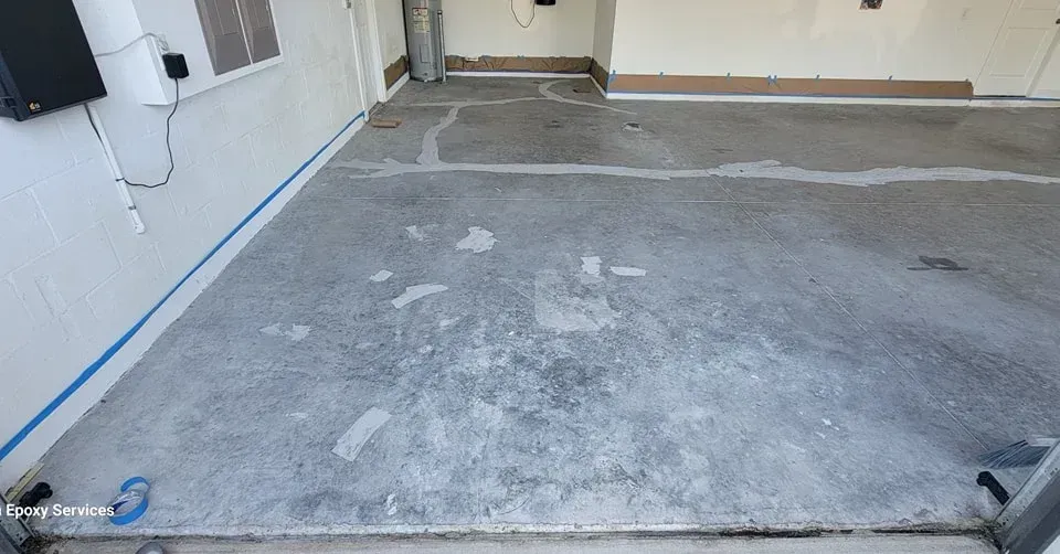 Concrete garage floor with patching and blue tape along the wall.