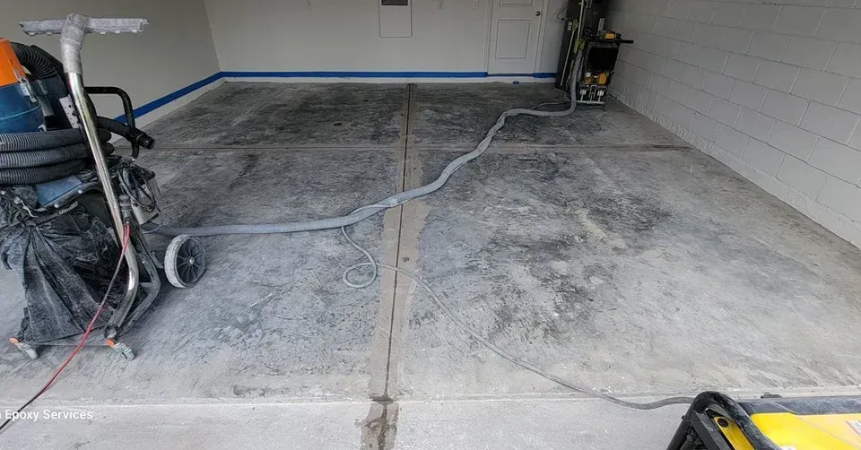 Floor grinding in progress; gray concrete floor, hose, machinery, and equipment inside a garage.
