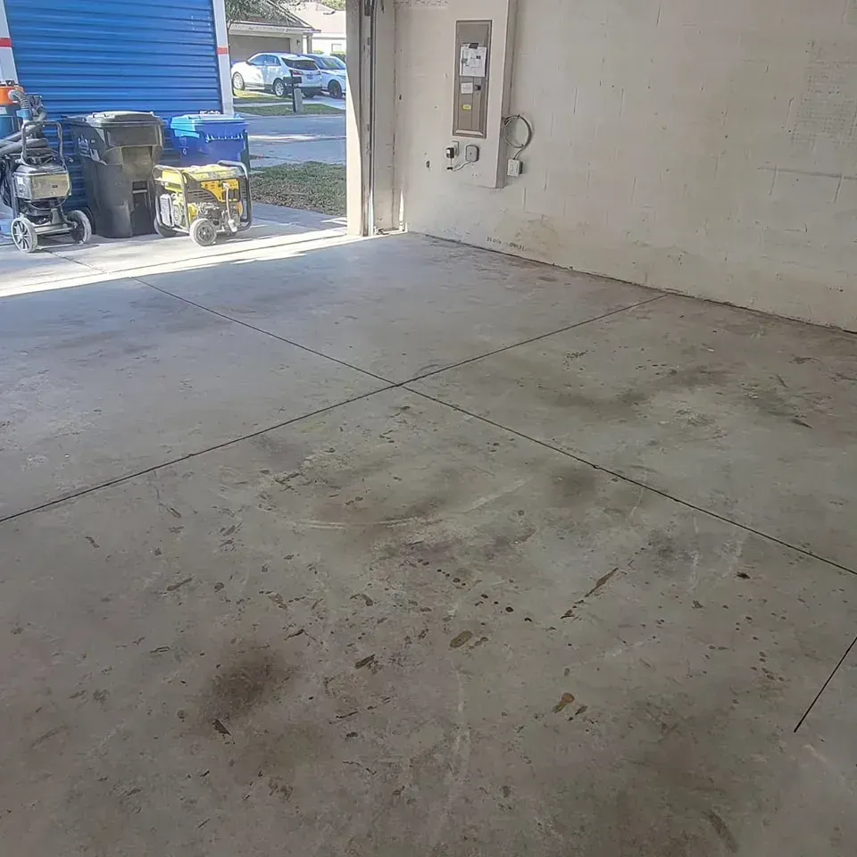 A concrete floor of a garage, marked with lines, partially open to the outdoors, with equipment inside and out.
