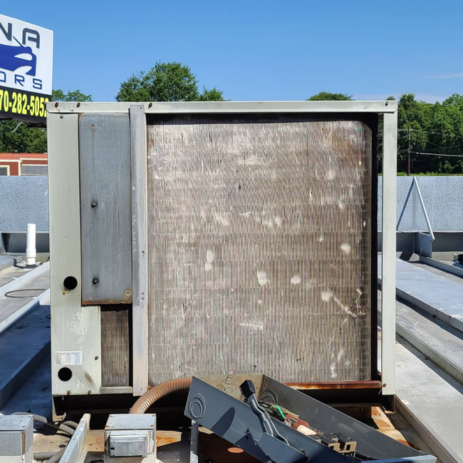 Outdoor HVAC unit with a large metal coil on a rooftop beside debris and a fence.