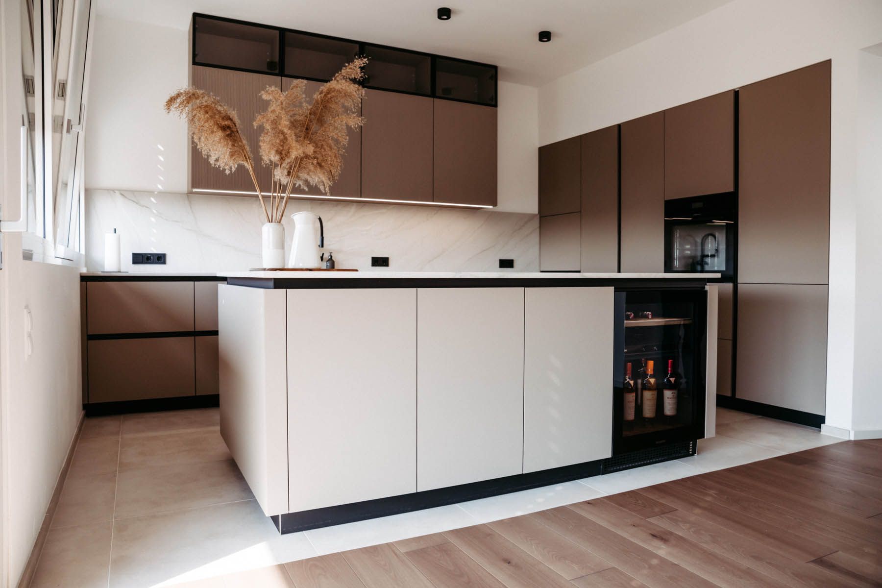 Moderne Küche mit beigen und braunen Schränken, einer Kochinsel und einem Weinkühlschrank.