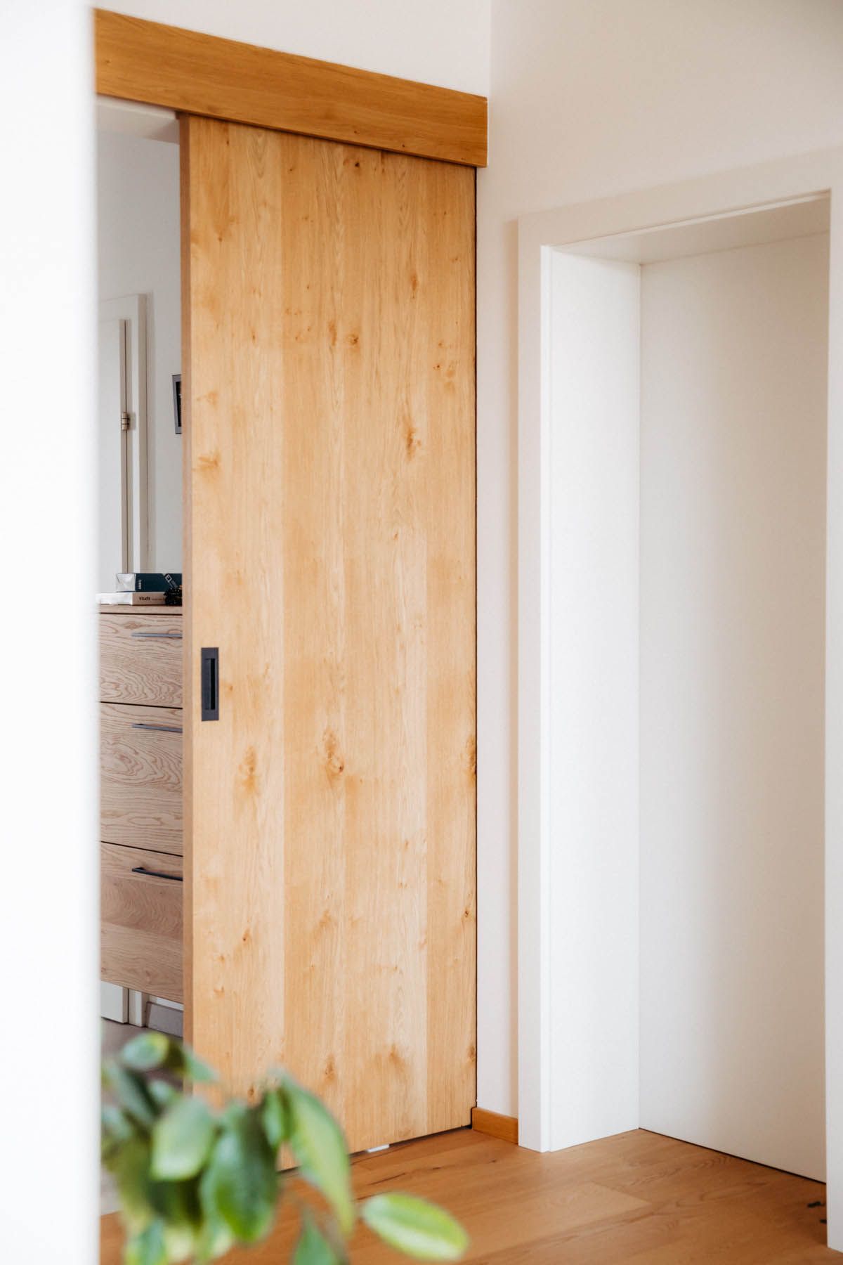 Eine Holzschiebetür führt in einen Raum mit hellem Holzboden und einer Kommode.