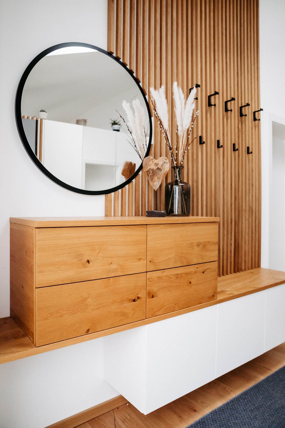 Ein moderner Eingangsbereich mit einem Holzschrank, einem runden Spiegel und einer dekorativen Wand mit Haken.