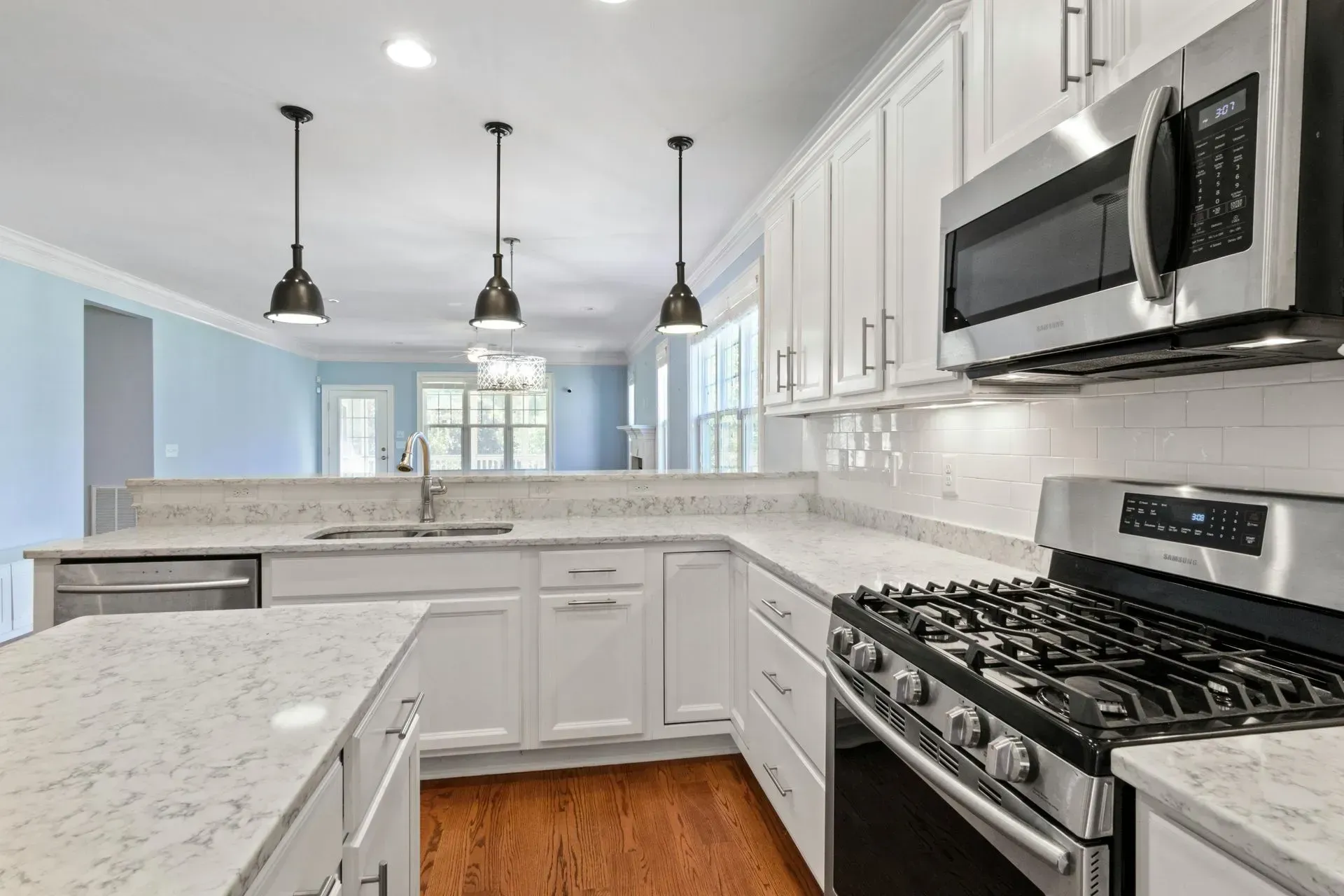 Bright white kitchen with marble countertops, stainless steel appliances, and black pendant lights