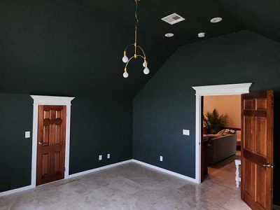 An empty room with dark walls and wooden doors and a chandelier hanging from the ceiling.