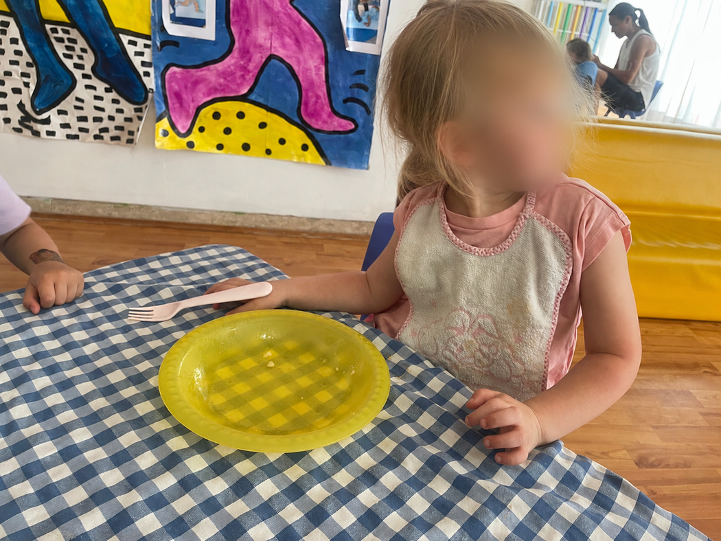 Bambino seduto a un tavolo con un piatto giallo in una stanza colorata