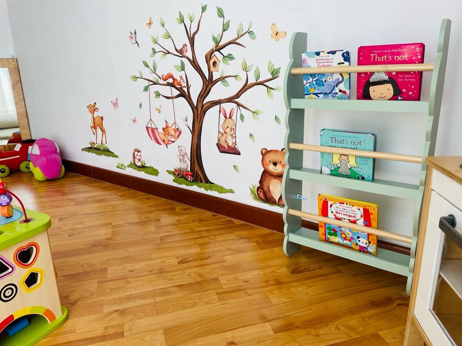 Quattro bambini seduti su panchine in un parco giochi che fanno gesti con le mani, con alberi e una recinzione sullo sfondo.