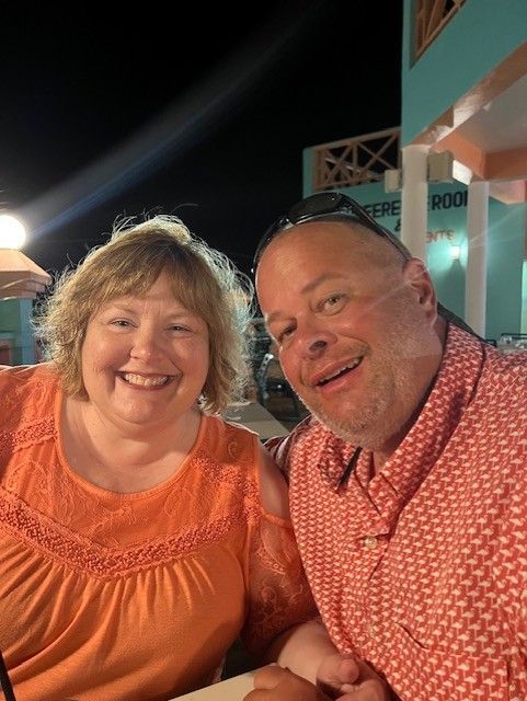 Two smiling people at an outdoor dinner, wearing orange and red patterned tops at night.