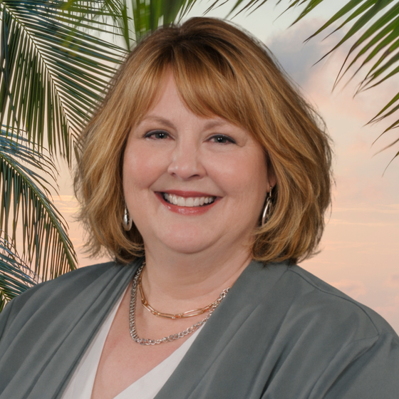 Smiling woman in a gray blouse with palm leaves in the background
