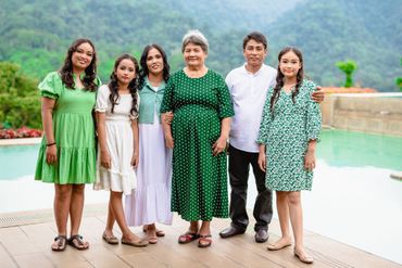Six people standing by a pool, smiling in coordinated green and white outfits with mountains behind them