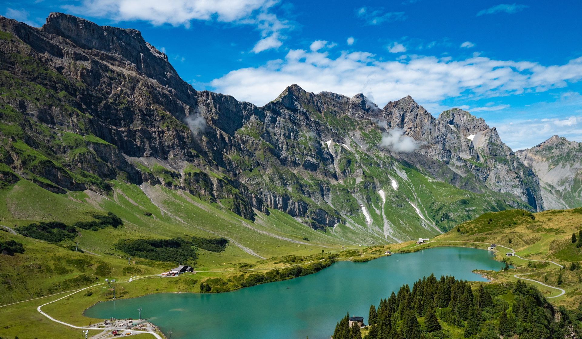 Turquoise alpine lake beside rocky mountains and green meadows under a blue sky