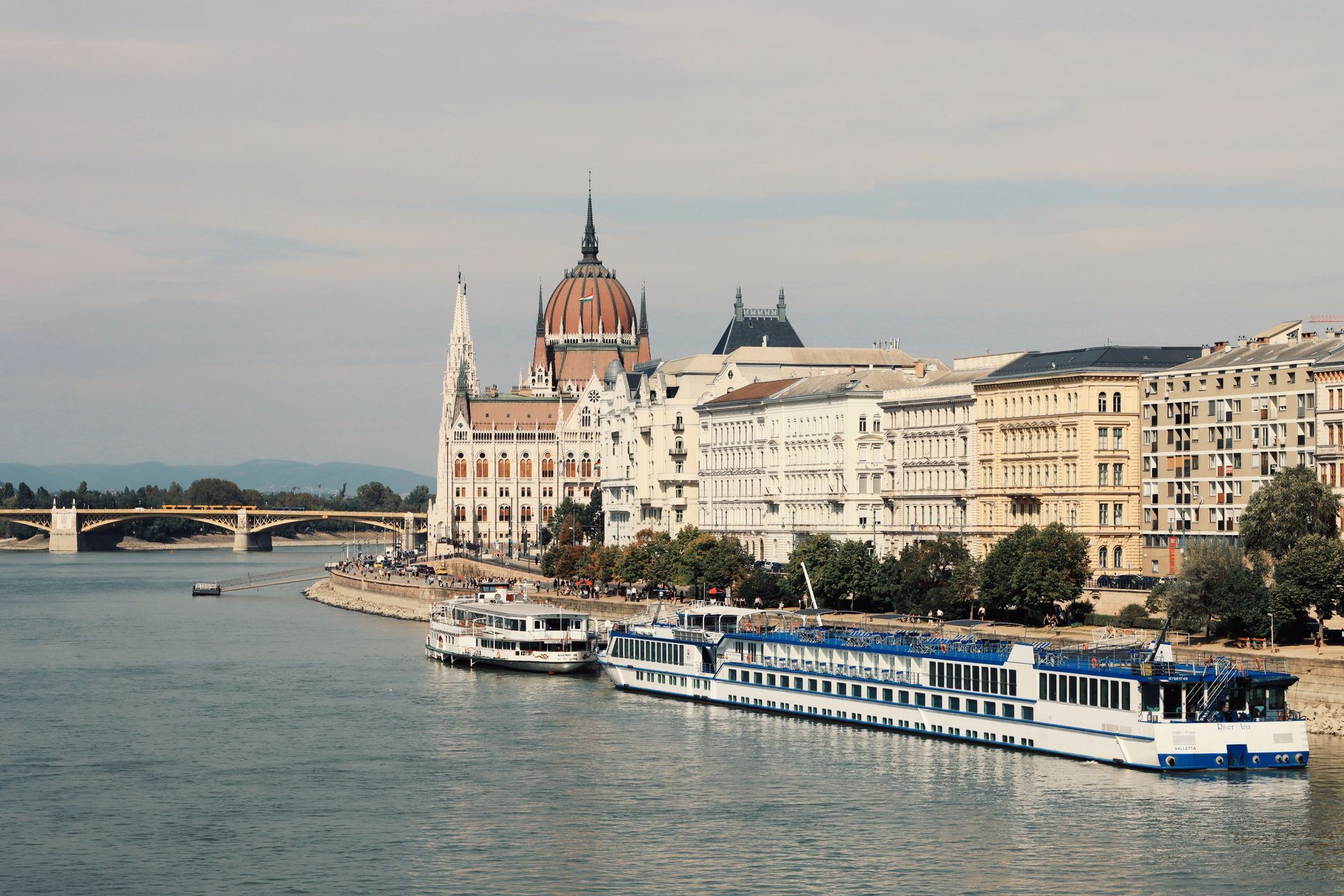 Riverfront cityscape with ornate historic buildings and a blue-and-white boat on the water