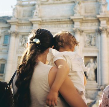 Woman holding a child in front of a sunlit white stone building