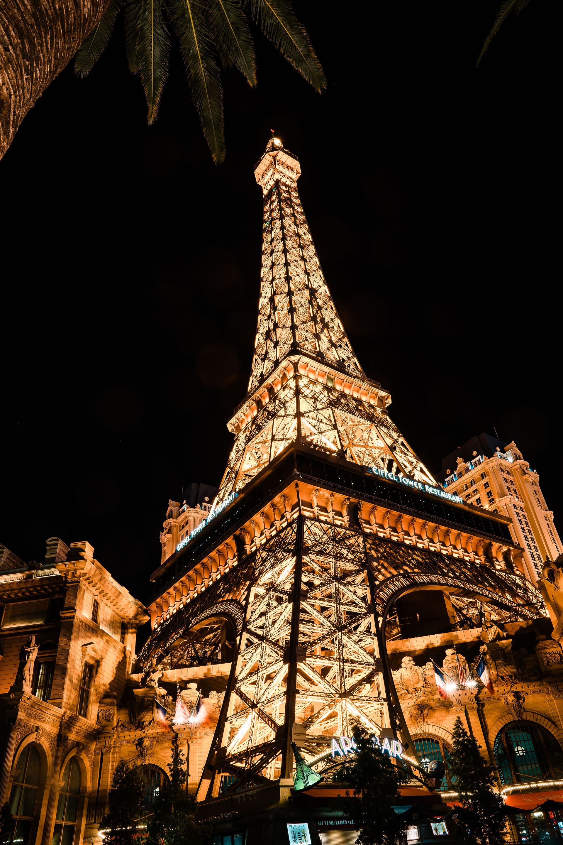 Lit Eiffel Tower replica glowing at night, surrounded by trees and adjacent buildings