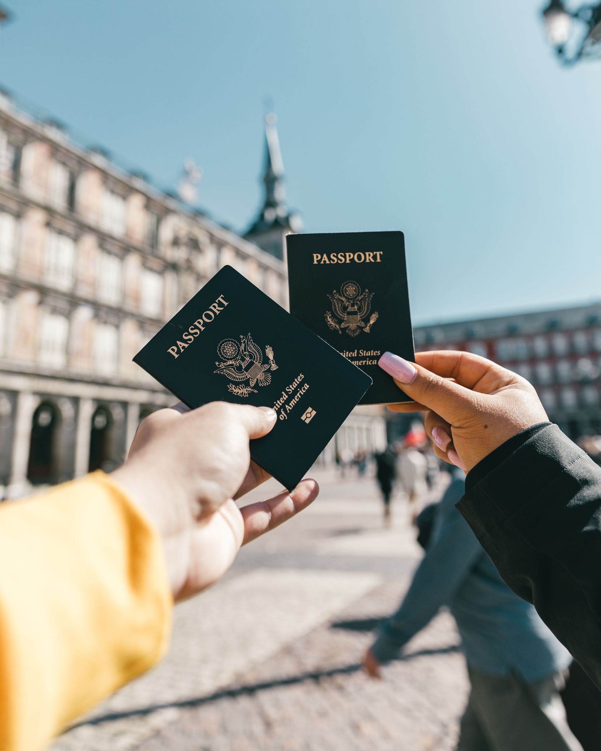 Three passports held up in a plaza with a historic building in the background
