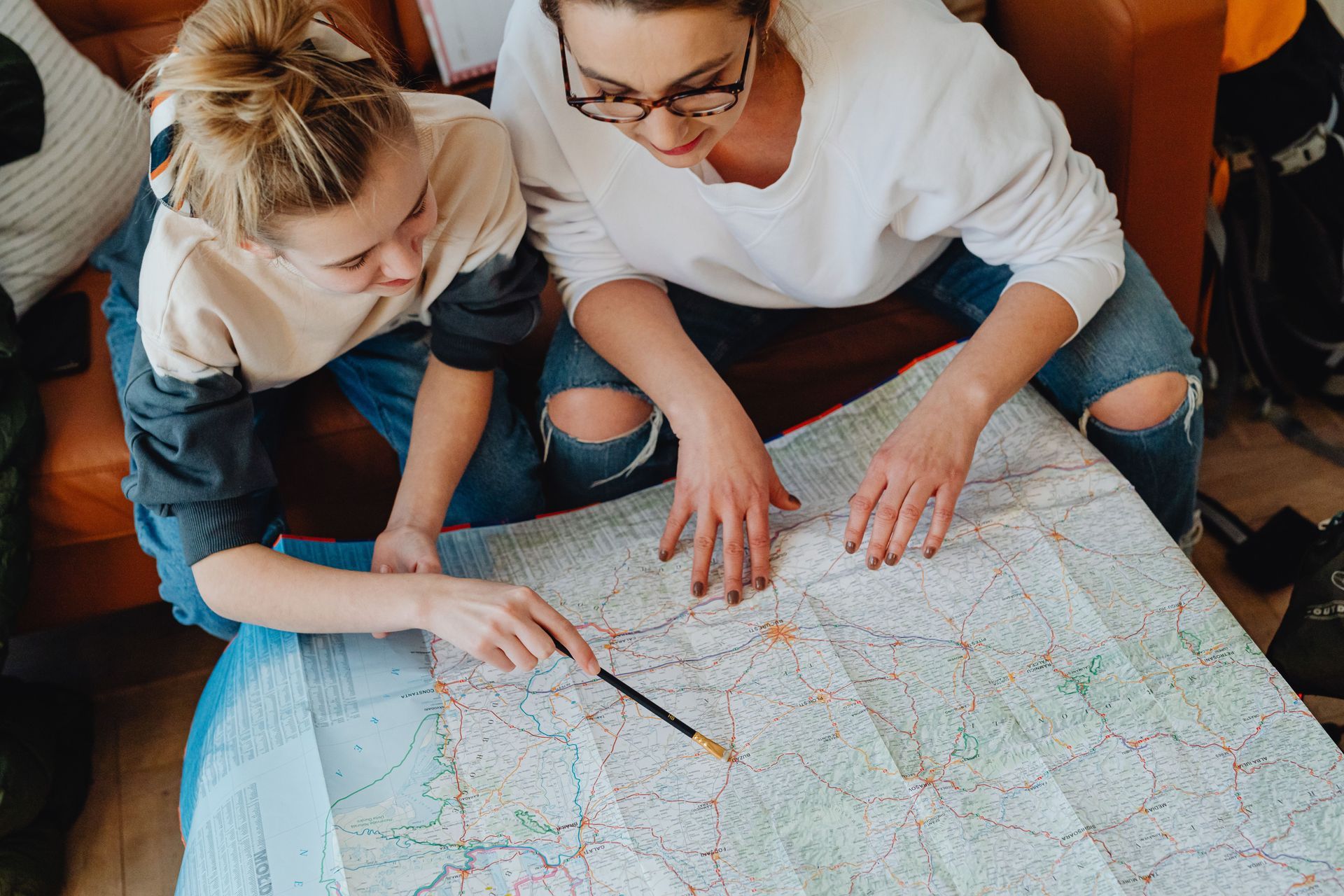 Two people pointing at a large map spread on a table, planning a route