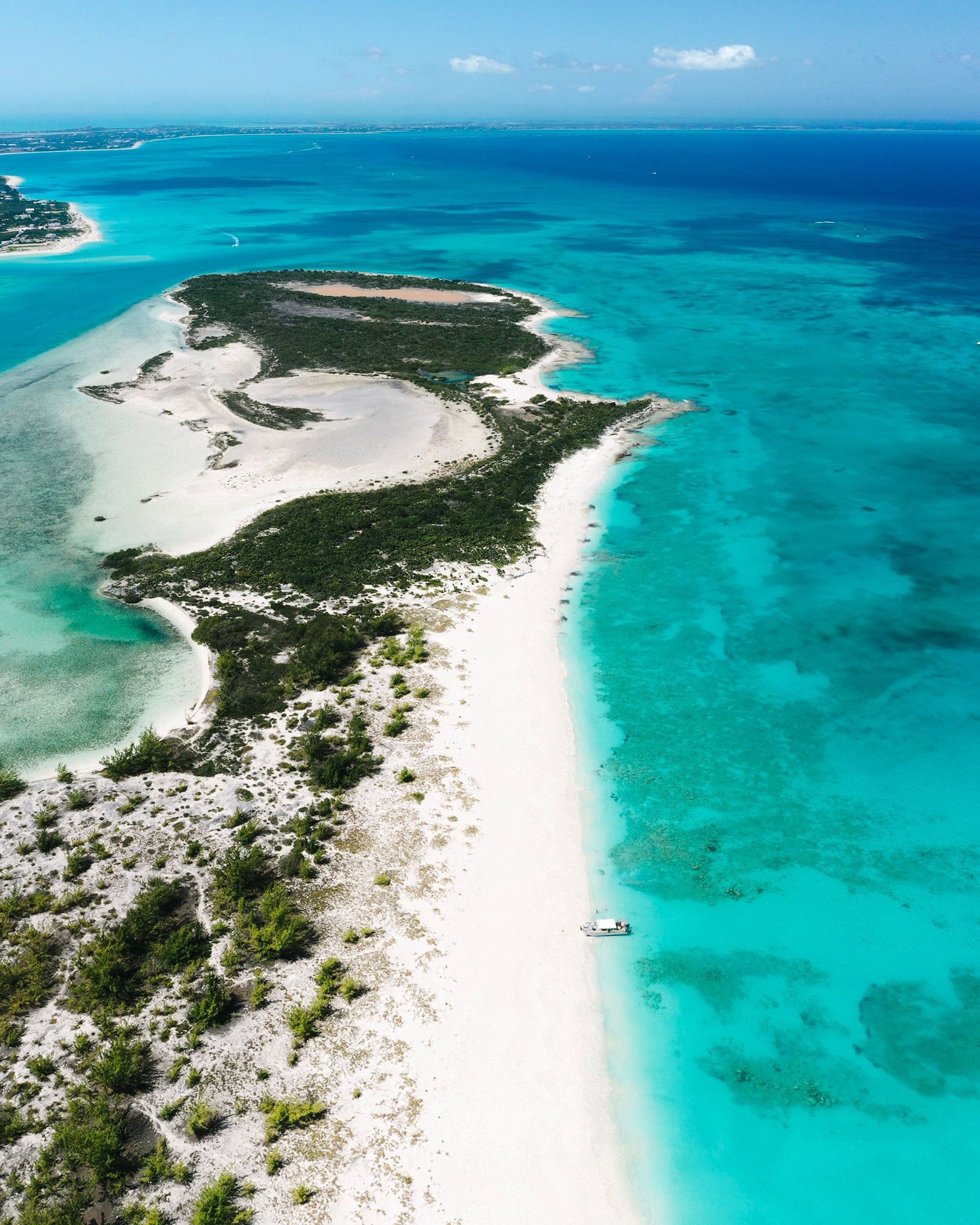Aerial view of a white sand island surrounded by turquoise blue ocean and coral reef.