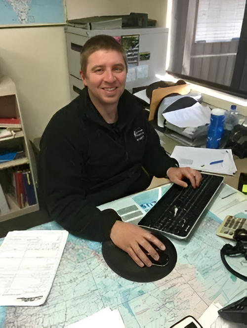 Man Smiling at a Desk With a Keyboard, Map, and Mouse, Indoors Near a Window — Dawson's Removals In Kelso, NSW