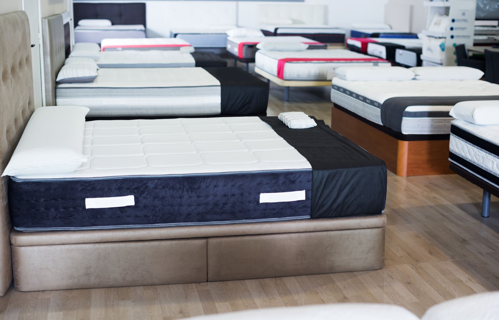 Mattresses displayed in a showroom, with beds arranged in rows on wood flooring.