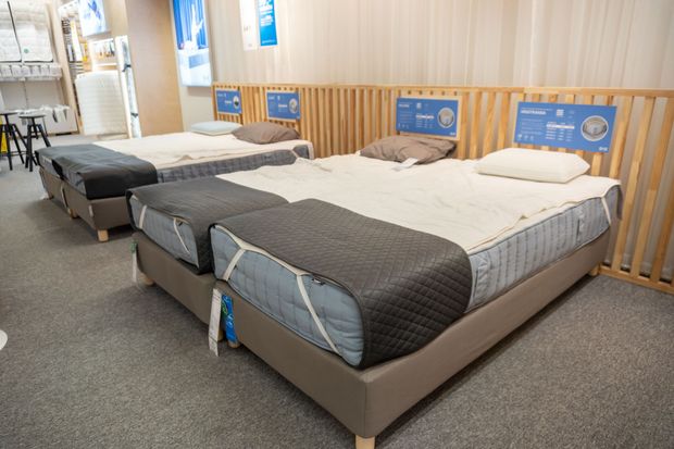 Three neatly made beds in a showroom with blue headboard signs and gray carpet