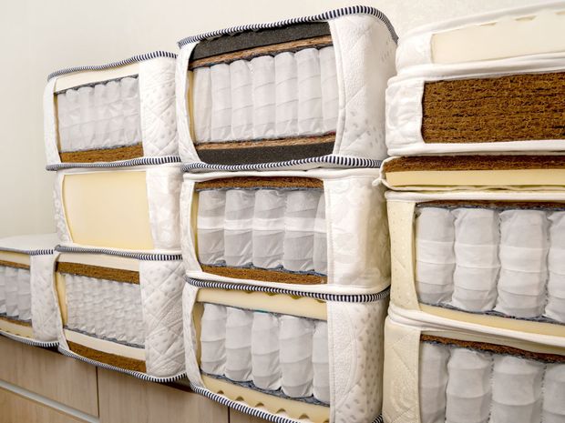 Stacked mattresses in white covers on store shelves, with beige and brown trim