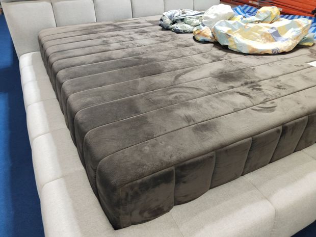 Gray upholstered bed with rumpled blankets and pillows in a bedroom