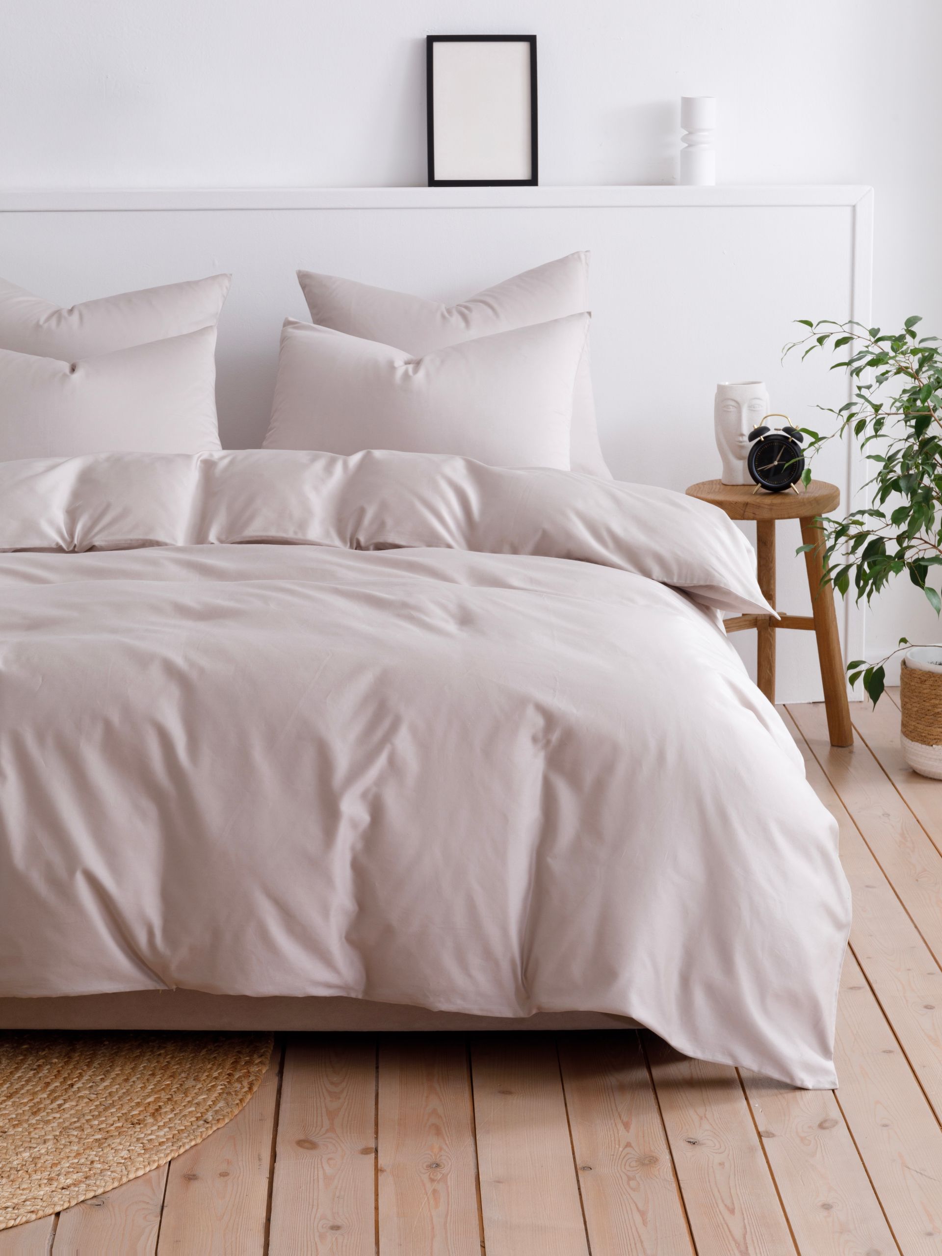 Minimalist bedroom with white bedding, wooden floor, small table, and potted plant by the bed