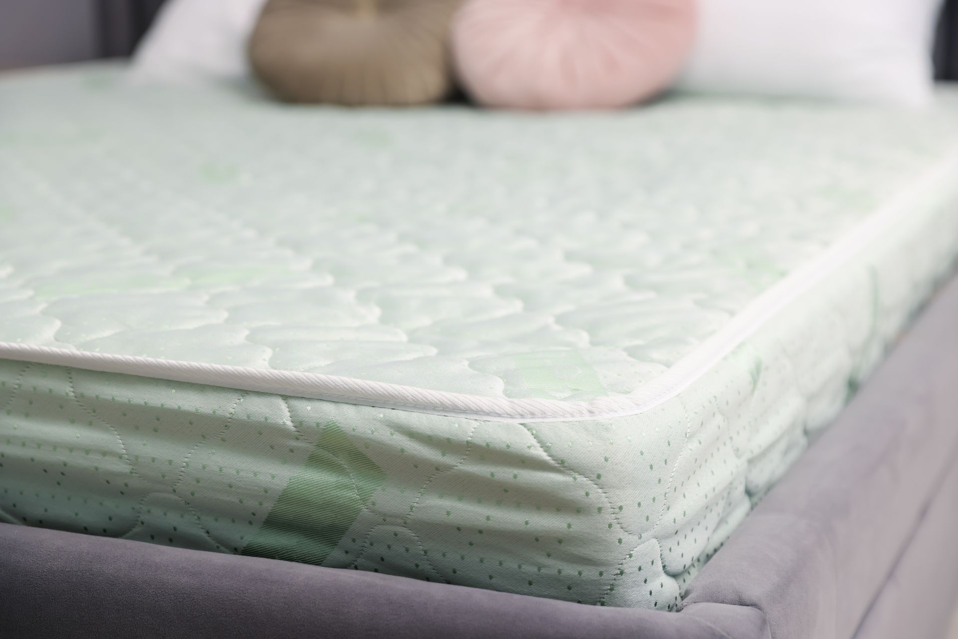 Close-up of a mint green mattress with floral pattern and stitched edge on a bed frame.