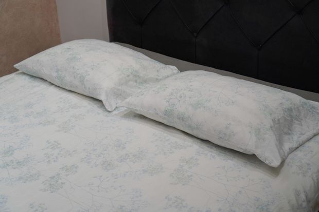 Two white pillows on a bed with a light floral bedspread and dark tufted headboard