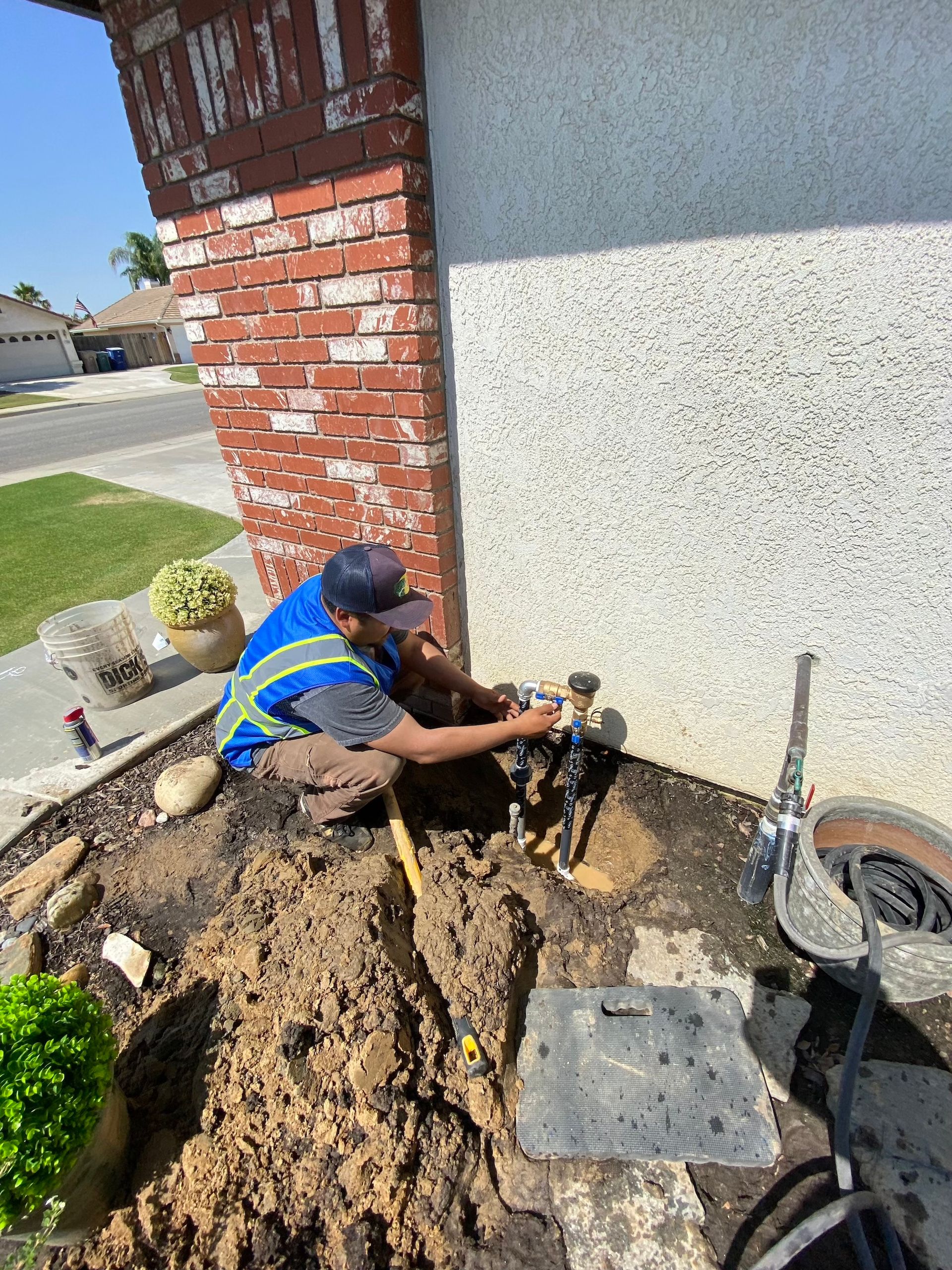 Man installing sprinkler system components near a house corner.