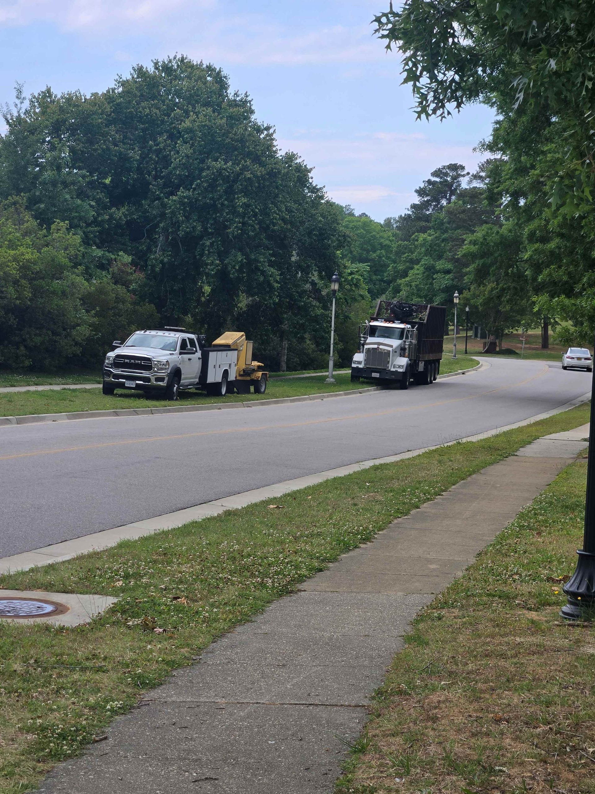 Two utility trucks parked on a tree-lined residential street beside a sidewalk.