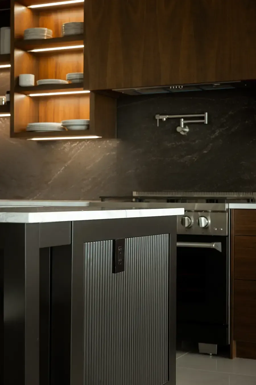 Modern kitchen featuring dark wood cabinets, a large granite island with white chairs, and hanging pendant lights.
